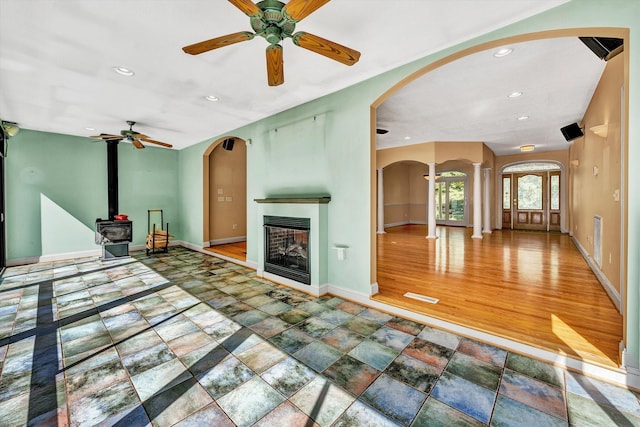 unfurnished living room featuring a wood stove, ceiling fan, wood-type flooring, and a multi sided fireplace