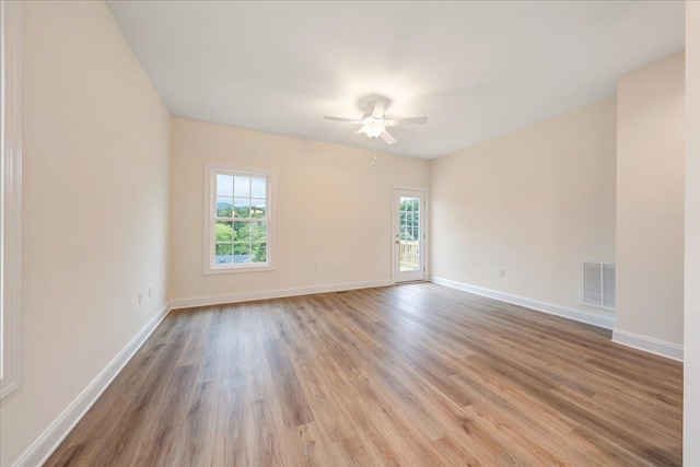 empty room with a ceiling fan, wood finished floors, visible vents, and baseboards