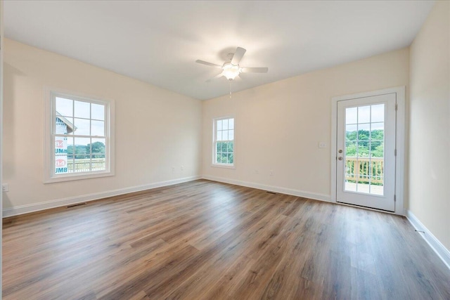 empty room featuring a ceiling fan, visible vents, baseboards, and wood finished floors