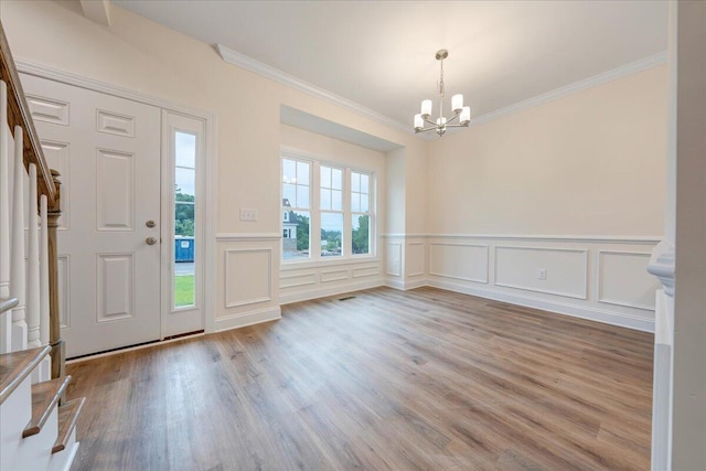 foyer featuring a wainscoted wall, wood finished floors, an inviting chandelier, stairs, and crown molding