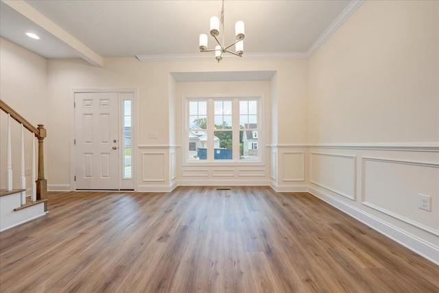 foyer entrance featuring wood finished floors, an inviting chandelier, stairs, crown molding, and a decorative wall