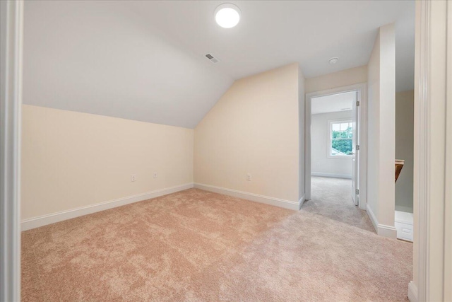 additional living space with light carpet, visible vents, baseboards, and vaulted ceiling