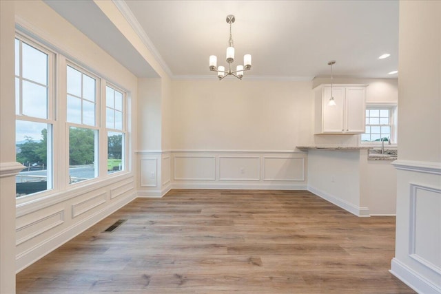 unfurnished dining area with a notable chandelier, wood finished floors, visible vents, and crown molding