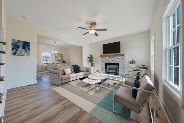 living room with ceiling fan with notable chandelier, a fireplace, and light hardwood / wood-style flooring