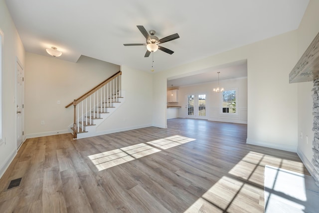 unfurnished living room with ceiling fan with notable chandelier and light hardwood / wood-style floors