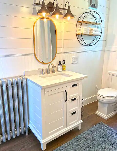 bathroom with toilet, wooden walls, vanity, wood-type flooring, and radiator