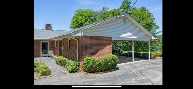 view of home's exterior featuring a chimney, a carport, and brick siding