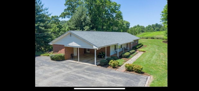 view of front of home with fence, aphalt driveway, a front yard, brick siding, and a carport
