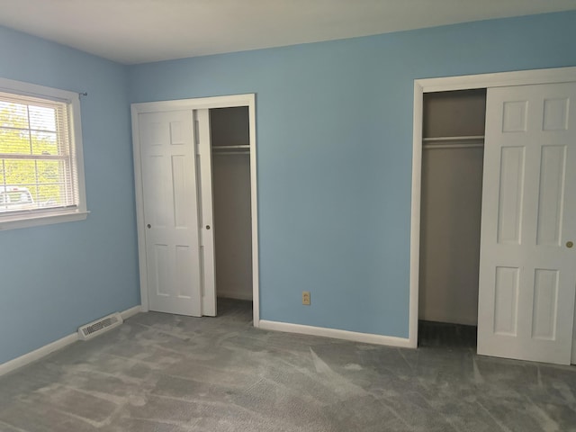 unfurnished bedroom featuring baseboards, carpet flooring, visible vents, and two closets