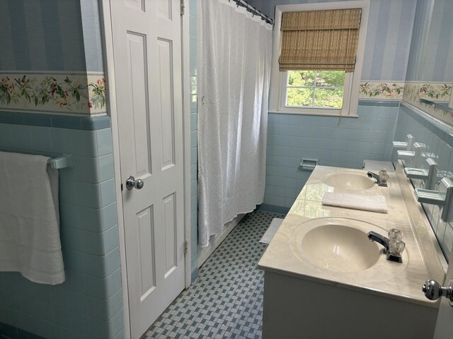 bathroom featuring double vanity, wallpapered walls, a sink, and wainscoting