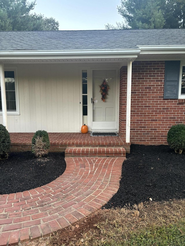 view of exterior entry featuring brick siding and roof with shingles