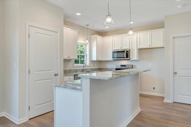 kitchen featuring light stone countertops, light hardwood / wood-style flooring, appliances with stainless steel finishes, a center island, and white cabinetry