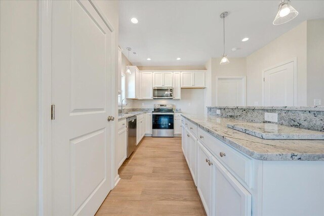 kitchen with white cabinetry, light hardwood / wood-style flooring, decorative light fixtures, light stone counters, and appliances with stainless steel finishes