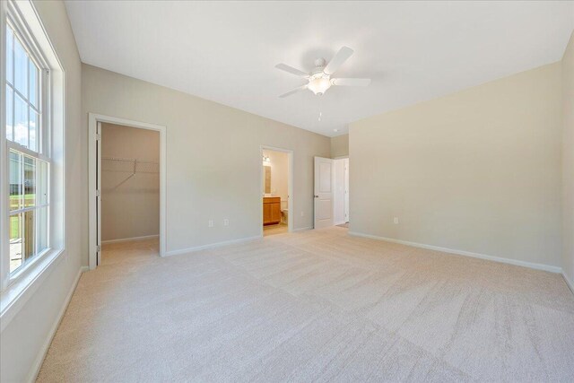 unfurnished bedroom with ensuite bathroom, light colored carpet, a closet, a spacious closet, and ceiling fan