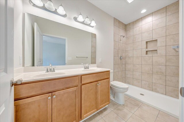 bathroom featuring vanity, toilet, a tile shower, and tile patterned floors