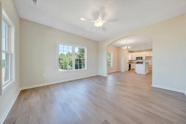 unfurnished living room featuring ceiling fan with notable chandelier, light hardwood / wood-style flooring, and a healthy amount of sunlight