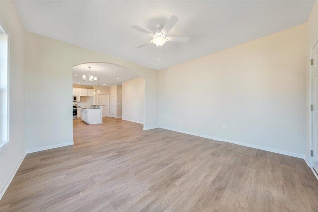 unfurnished living room featuring ceiling fan with notable chandelier and light hardwood / wood-style flooring