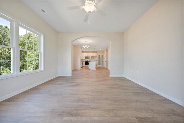 unfurnished living room with ceiling fan with notable chandelier and light hardwood / wood-style floors