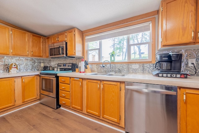 kitchen with appliances with stainless steel finishes, light hardwood / wood-style floors, sink, and a wealth of natural light