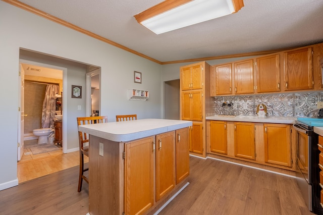 kitchen featuring stainless steel electric stove, a breakfast bar area, ornamental molding, a center island, and light wood-type flooring