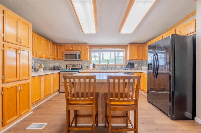 kitchen with a breakfast bar, a center island, light hardwood / wood-style flooring, appliances with stainless steel finishes, and backsplash