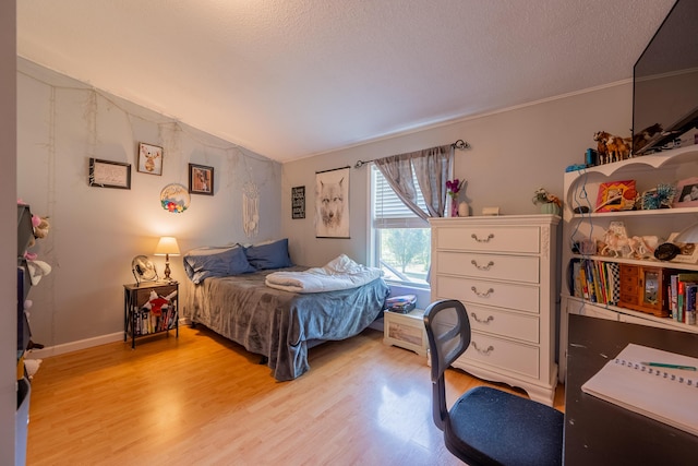 bedroom featuring lofted ceiling, light hardwood / wood-style flooring, and a textured ceiling