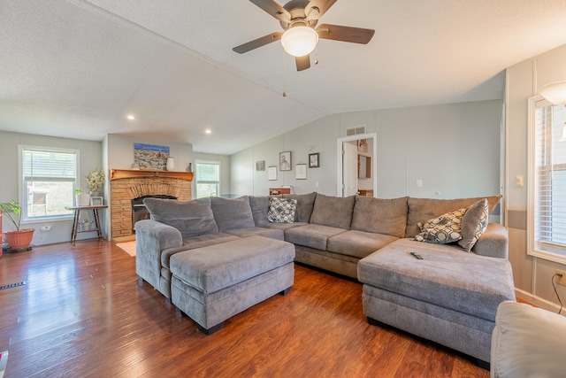 living room with lofted ceiling, dark hardwood / wood-style floors, a stone fireplace, and ceiling fan