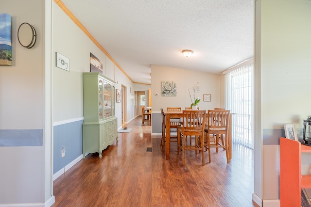 dining space with lofted ceiling, crown molding, dark hardwood / wood-style floors, and a textured ceiling