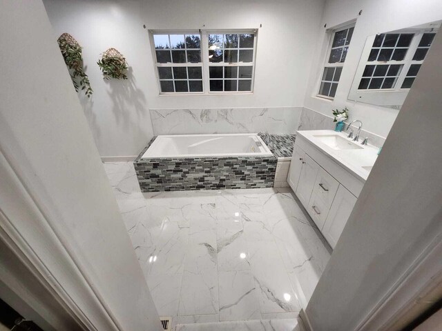 bathroom featuring tiled tub and vanity