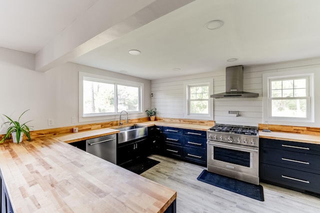 kitchen featuring light wood-type flooring, stainless steel appliances, sink, wall chimney range hood, and butcher block counters