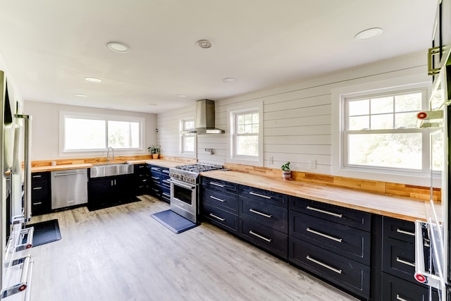 kitchen with light wood-type flooring, stainless steel appliances, wood counters, sink, and wall chimney range hood