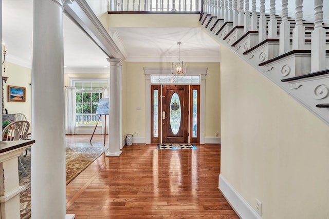 foyer entrance with decorative columns, a chandelier, wood-type flooring, and crown molding