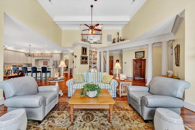 living room with wood-type flooring, crown molding, ornate columns, and ceiling fan with notable chandelier