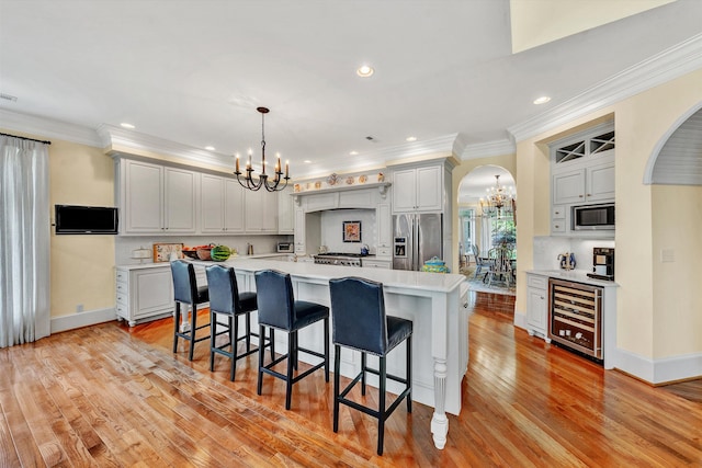 kitchen with beverage cooler, light hardwood / wood-style flooring, pendant lighting, appliances with stainless steel finishes, and a large island with sink