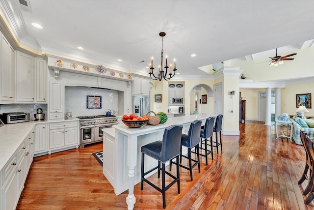 kitchen with appliances with stainless steel finishes, decorative light fixtures, light hardwood / wood-style floors, a breakfast bar, and a center island