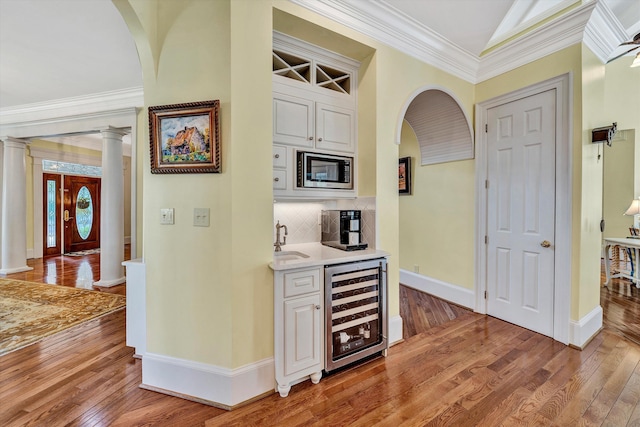 bar featuring wood-type flooring, ornamental molding, wine cooler, and tasteful backsplash