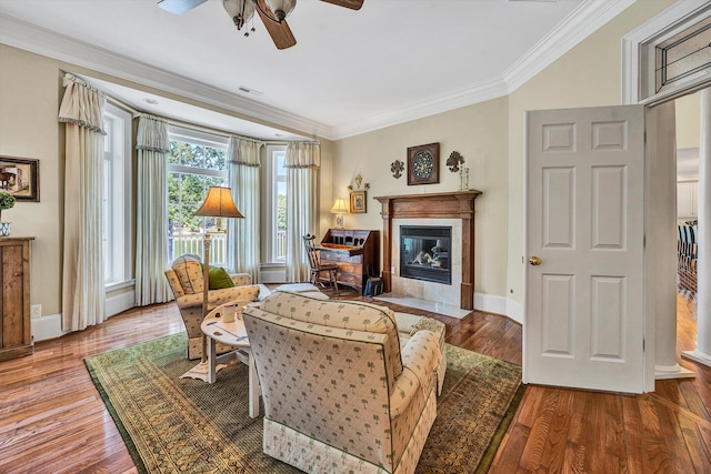 living room featuring wood-type flooring, a tile fireplace, ceiling fan, and crown molding