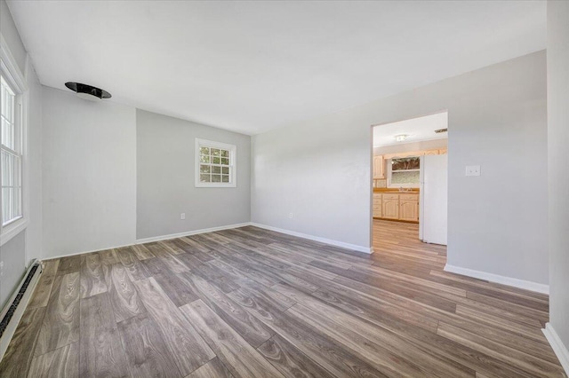 unfurnished room featuring a baseboard heating unit, a healthy amount of sunlight, and hardwood / wood-style floors