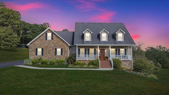 new england style home featuring covered porch and a lawn