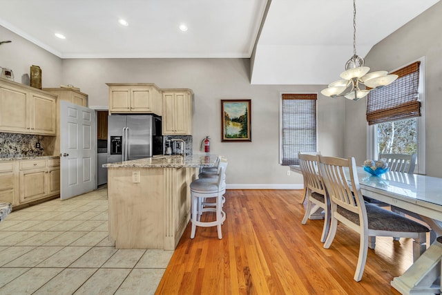 kitchen with light wood-type flooring, a chandelier, a kitchen bar, kitchen peninsula, and stainless steel fridge with ice dispenser