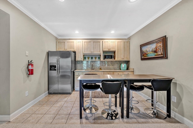 kitchen featuring ornamental molding, backsplash, light tile patterned floors, stainless steel appliances, and a breakfast bar area