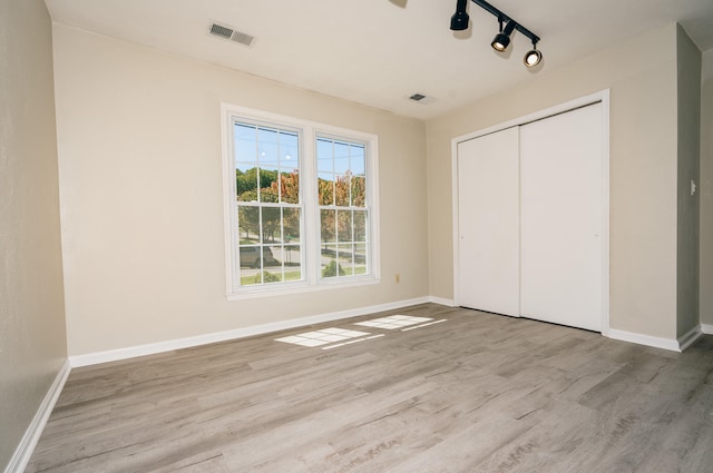 unfurnished bedroom with rail lighting, a closet, and light hardwood / wood-style flooring