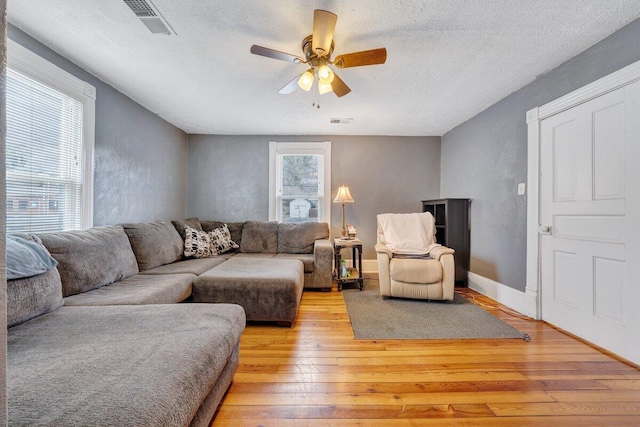 living room featuring light hardwood / wood-style floors, ceiling fan, and a textured ceiling