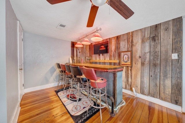 bar featuring hardwood / wood-style flooring, wood walls, and ceiling fan