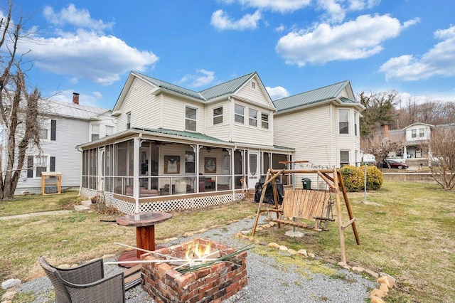 back of property with a yard, a sunroom, and an outdoor fire pit