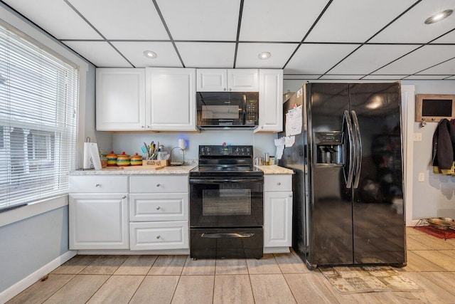 kitchen with a drop ceiling, white cabinetry, light stone countertops, and black appliances