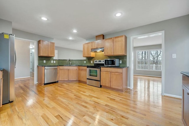 kitchen featuring a sink, appliances with stainless steel finishes, light wood-type flooring, decorative backsplash, and dark stone countertops