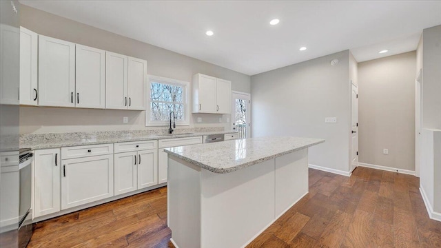 kitchen featuring light stone counters, a kitchen island, a sink, and white cabinets