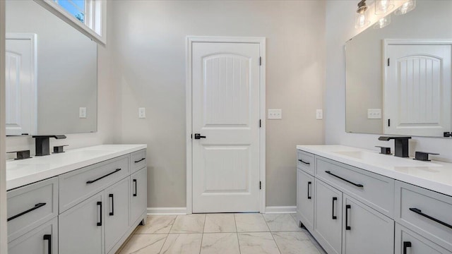 full bath featuring marble finish floor, baseboards, two vanities, and a sink