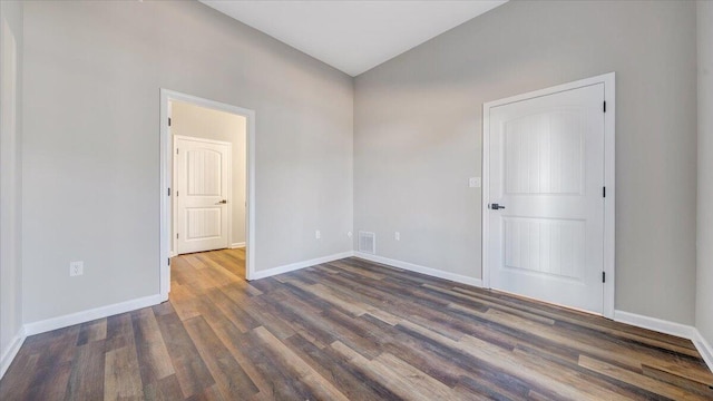 empty room with dark wood finished floors, visible vents, vaulted ceiling, and baseboards